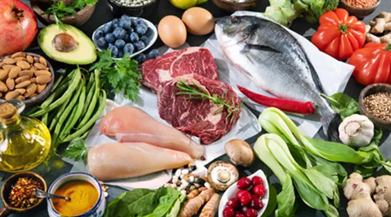 A variety of fresh groceries and ingredients laid out on a table, including meat, fish, and vegetables.
